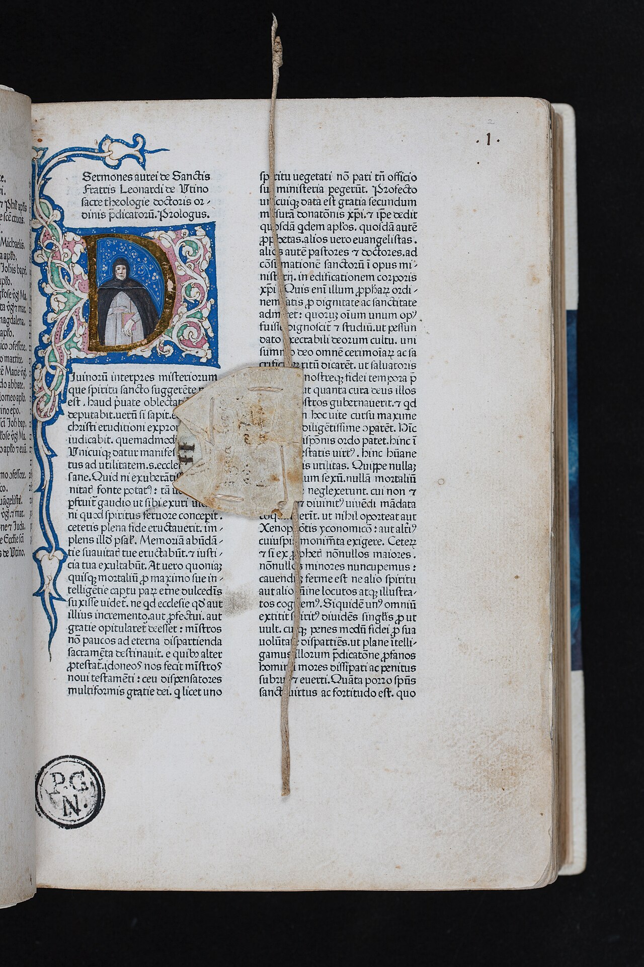 A fifteenth-century printed book open on an illuminated first page. From the top of the spine a cord drops down the middle of the leaf, carrying a small parchment marker that rests over a column of text.